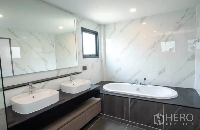 Detached House for rent in Bang Phli, Samut Prakan - Luxury bathroom with bathtub, double vanity and marble-style wall tiles.