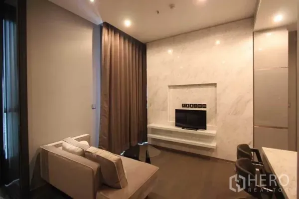 Condominium for rent in Huai Khwang, Bangkok - Living room with marble TV wall, sofa and curtains next to the kitchen bar.