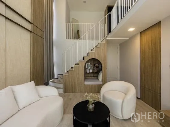 独栋房屋 for rent or sale in Saphan Sung, Bangkok - 挑高家庭厅带楼梯与楼梯下阅读壁龛，搭配现代沙发。