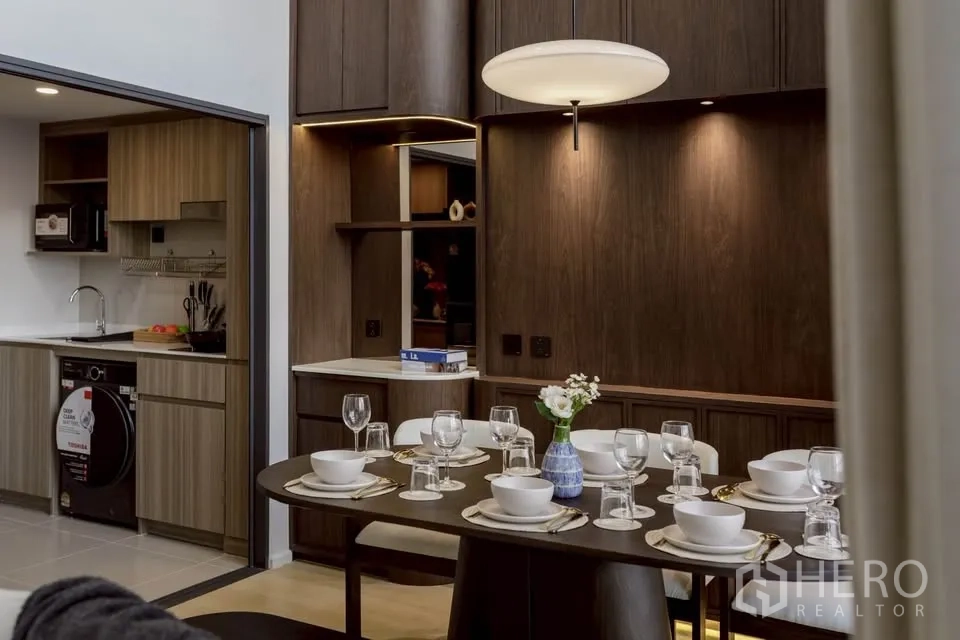 Condominium for rent in Khlong Toei, Bangkok - Modern kitchen with wood cabinets and built-in appliances beside a dining table set for six.