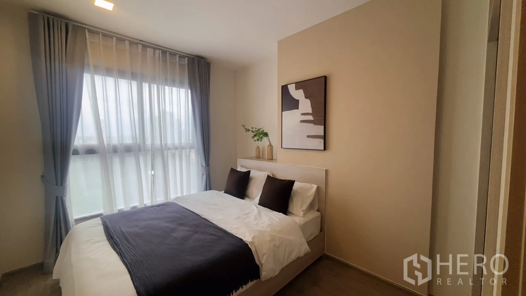 Condominium for rent in Watthana, Bangkok - Bedroom with double bed, soft furnishings, artwork above the headboard, and a tall window with sheer curtains.