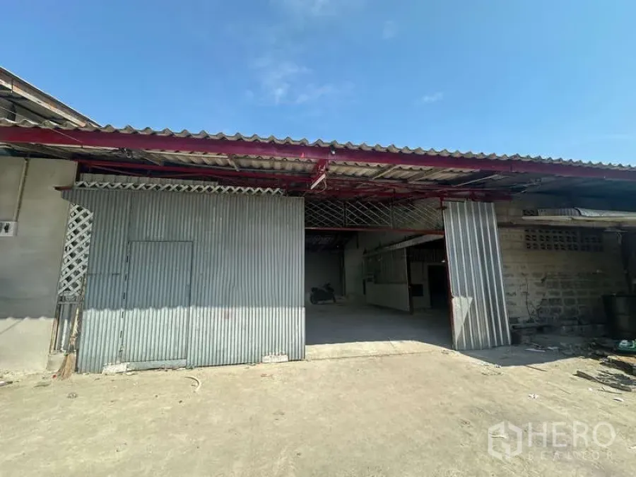 Warehouse for rent in Suan Luang, Bangkok - Corrugated metal warehouse exterior with sliding doors, covered loading bay and a paved forecourt under a clear sky.