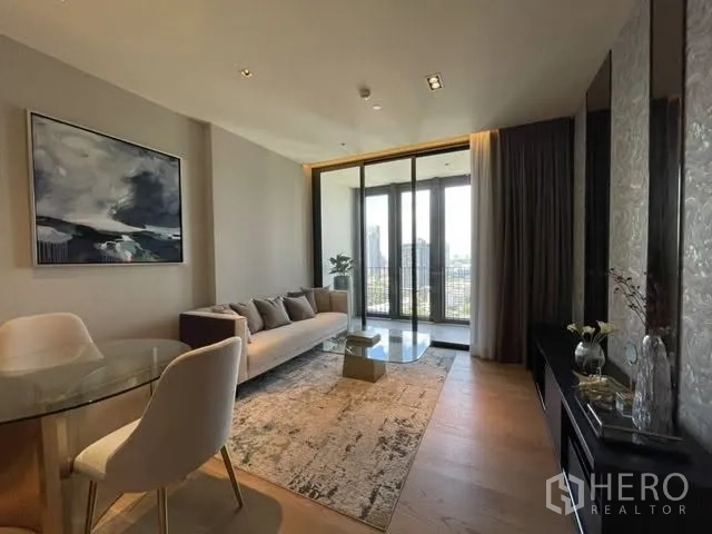 Condominium for rent or sale in Khlong Toei, Bangkok - Bright living area with sofa, round dining table, and floor-to-ceiling doors opening to a balcony with city views.