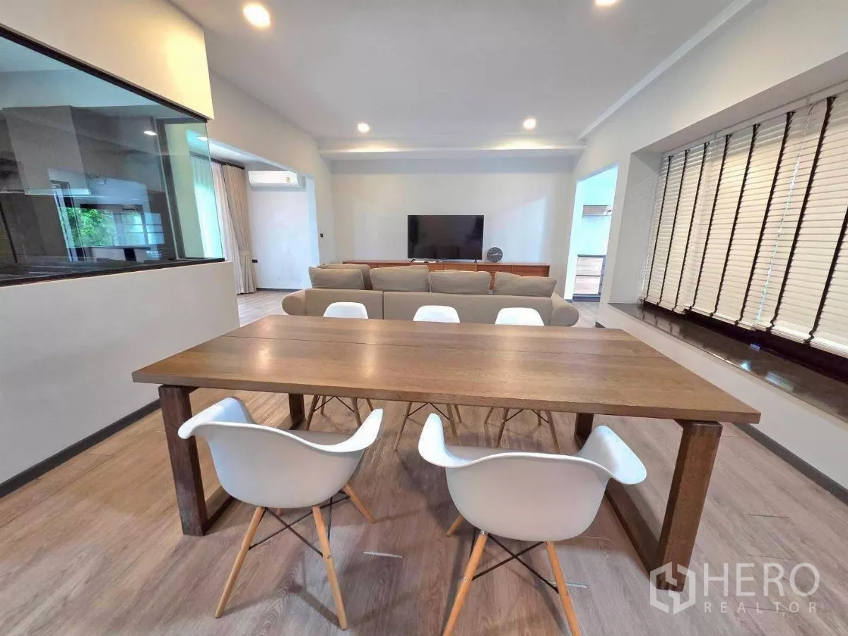 Detached House for rent in Bang Phli, Samut Prakan - Dining area with solid wood table and white chairs beside a large window and glass kitchen wall.