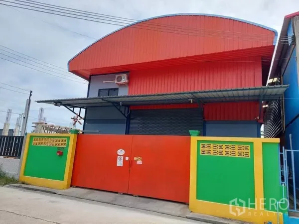 货栈 出租或出售在Bang Bua Thong, Nonthaburi - 彩色金属外墙仓库，红色拱形屋顶，宽卷帘门与安全大门。