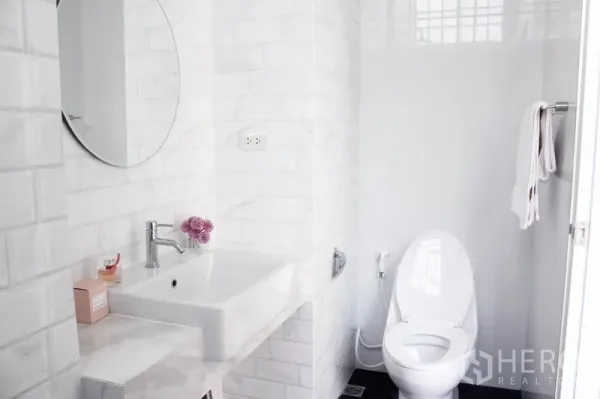 Home Office for rent in Khlong Toei, Bangkok - Modern bathroom with white subway tiles, round mirror, vanity sink and toilet.