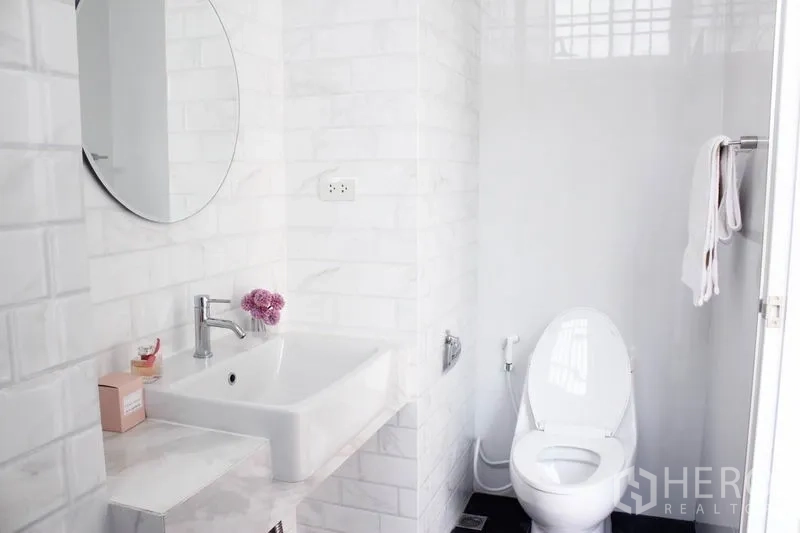 Home Office for rent in Khlong Toei, Bangkok - Modern bathroom with white subway tiles, round mirror, vanity sink and toilet.
