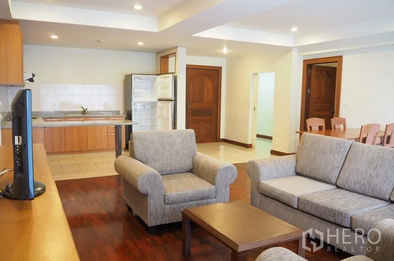 Condominium for rent in Pathum Wan, Bangkok - Open-plan living room with gray sofa set, wood floors and kitchen at the back