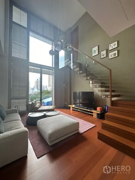 Condominium for rent or sale in Sathon, Bangkok - Another angle of living room highlighting floating stairs, sectional sofa, and TV.