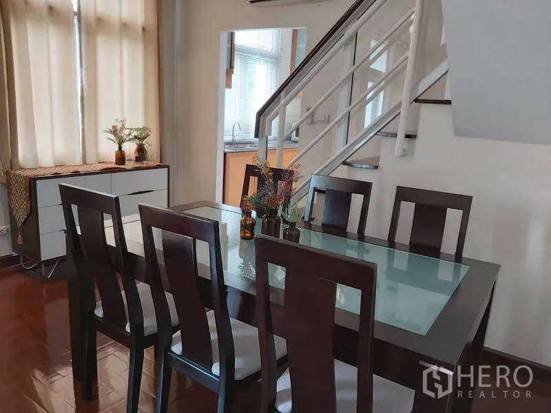 公寓 出租在Watthana, Bangkok - 餐区设六人玻璃餐桌，毗邻楼梯并靠近厨房。