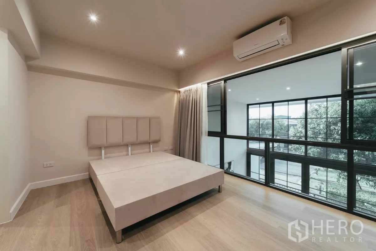 联排别墅 出租在Watthana, Bangkok - 卧室通过黑框玻璃俯瞰挑高餐区，配空调。