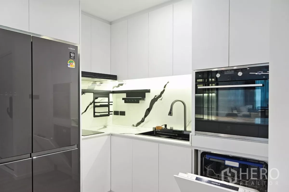 Condominium for rent in Watthana, Bangkok - Modern U-shaped kitchen with marble-look backsplash, induction hob, built-in oven, dishwasher and large fridge in the condominium.