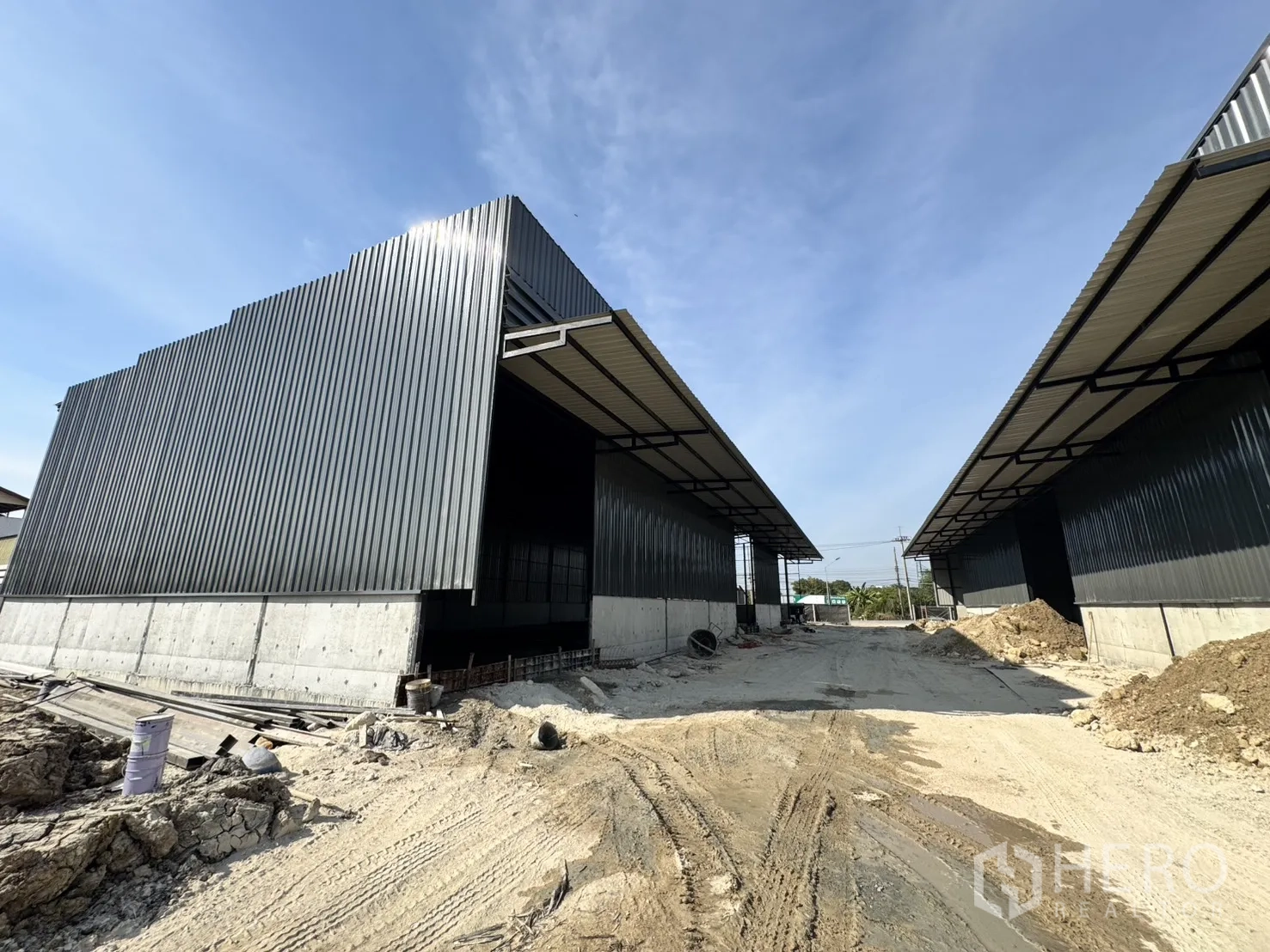 Warehouse for rent in Lam Luk Ka, Pathum Thani - Corrugated metal warehouse buildings with elevated concrete bases and a long loading lane.