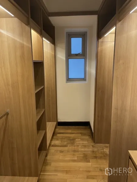 Condominium for rent or sale in Pathum Wan, Bangkok - Walk‑in closet with built‑in wooden shelving and hanging space, illuminated with a small window.
