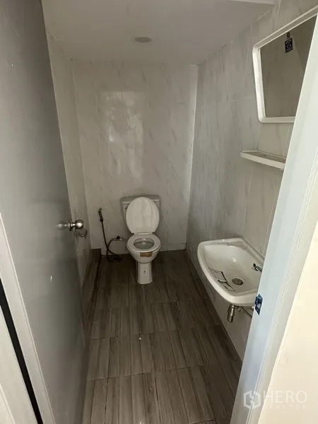 Warehouse for rent in Pathum Thani - Tiled restroom with toilet, sink and wall mirror inside the warehouse.