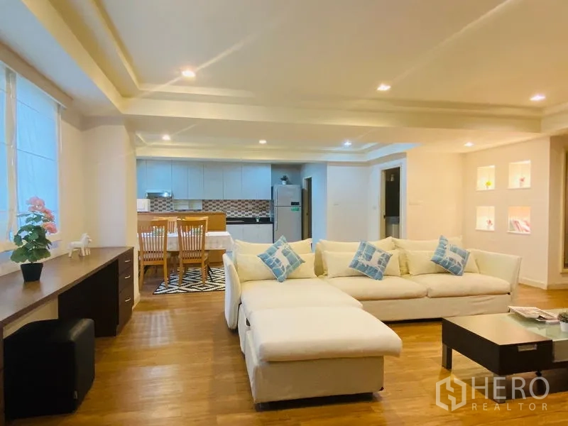 Condominium for rent in Watthana, Bangkok - Open living, dining and kitchen space featuring a white sectional with blue cushions, long work desk and stainless refrigerator.