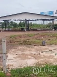 Land for sale in Mueang Samut Sakhon, Samut Sakhon - View across cleared land toward a steel‑frame shed behind a low fence.