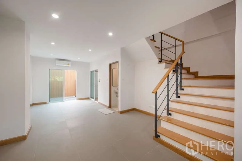 ทาวน์เฮาส์ ขายในLat Phrao, Bangkok - โถงชั้นล่างพร้อมบันไดไม้ ประตูบานเลื่อนไปยังลานด้านหลัง และเครื่องปรับอากาศ