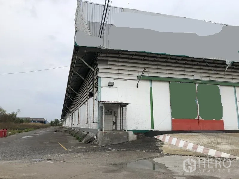 Warehouse for rent in Samut Prakan - Warehouse exterior corner with security post and large rolling doors.