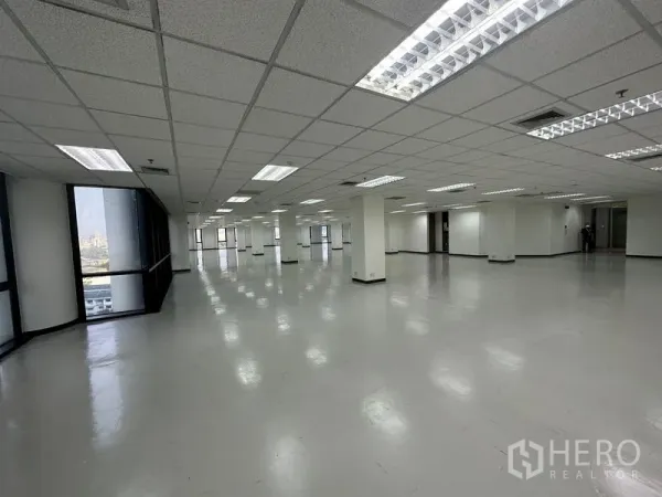 Office Space for rent - Large open-plan office floor with grid ceiling lights, columns, and big corner windows showing city views.