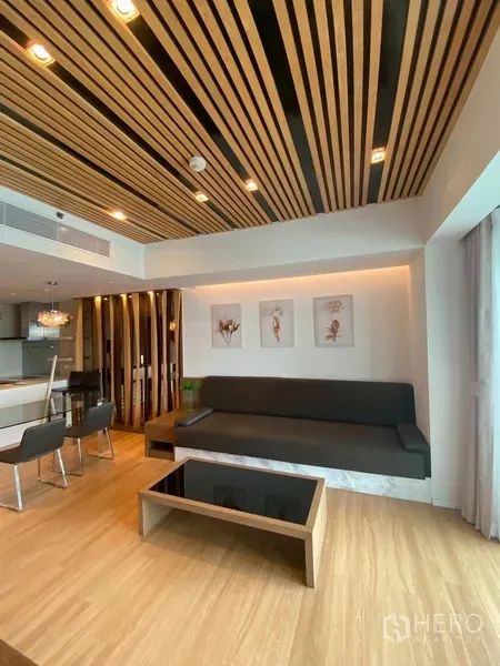 Condominium for rent in Yan Nawa, Bangkok - Modern lounge with wood-slat ceiling, built-in sofa and coffee table beside full-height windows.