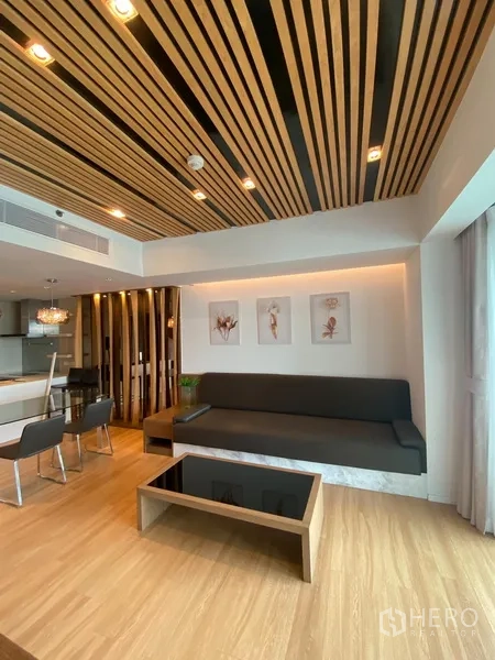 Condominium for rent in Yan Nawa, Bangkok - Modern lounge with wood-slat ceiling, built-in sofa and coffee table beside full-height windows.