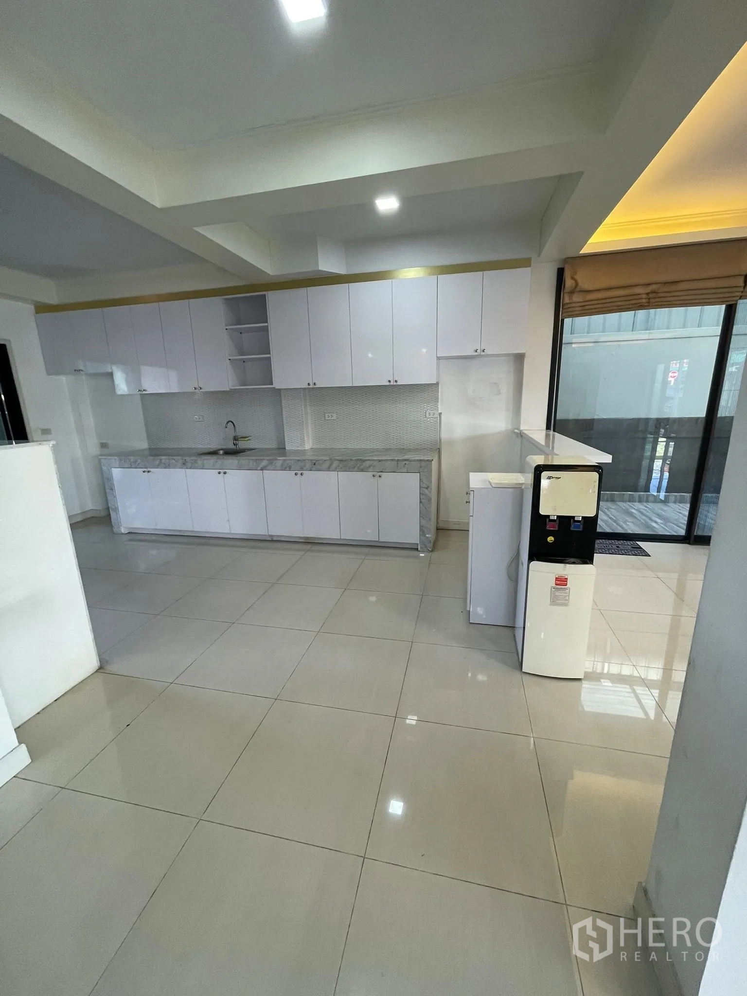 Detached House for rent or sale in Lam Luk Ka, Pathum Thani - Open kitchen and dining space with glossy floor tiles and a long counter.
