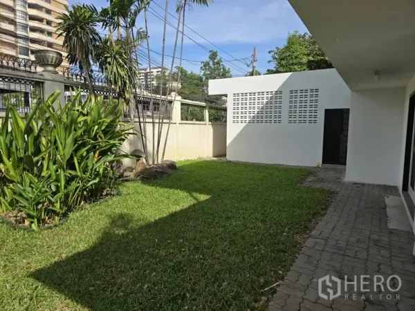 บ้าน ให้เช่าในWatthana, Bangkok - สนามหญ้าด้านข้างพร้อมทางเดิน ต้นปาล์ม และอาคารเอนกประสงค์สีขาวในรั้วบ้าน