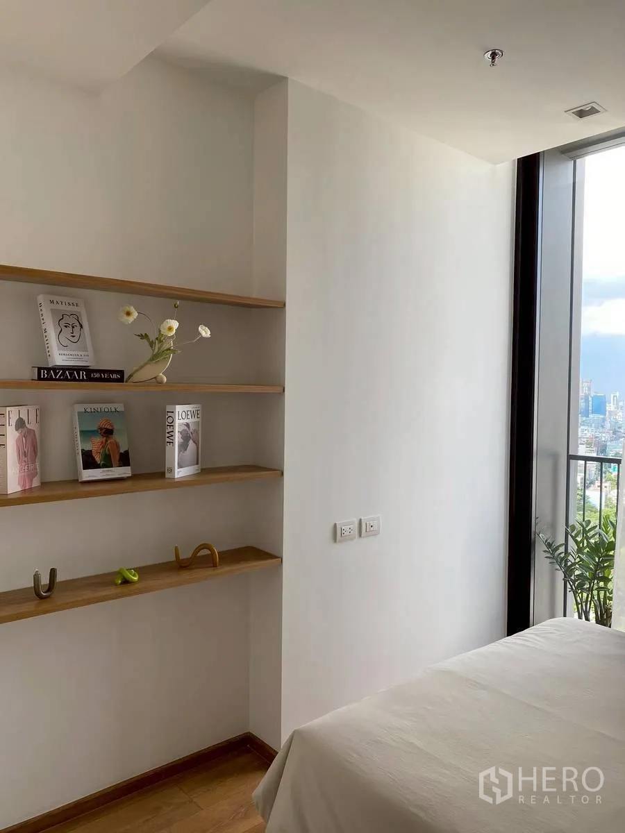 Condominium for rent in Watthana, Bangkok - Built-in wooden shelves and a large window beside the bed with skyline views.