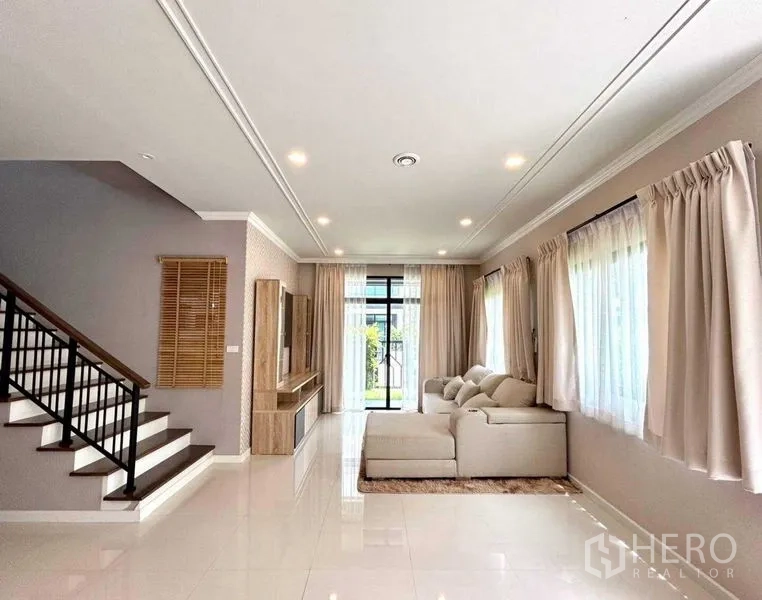 Detached House for rent in Khlong Sam Wa, Bangkok - Open-plan living area with stairs, sofa and full-height windows with curtains
