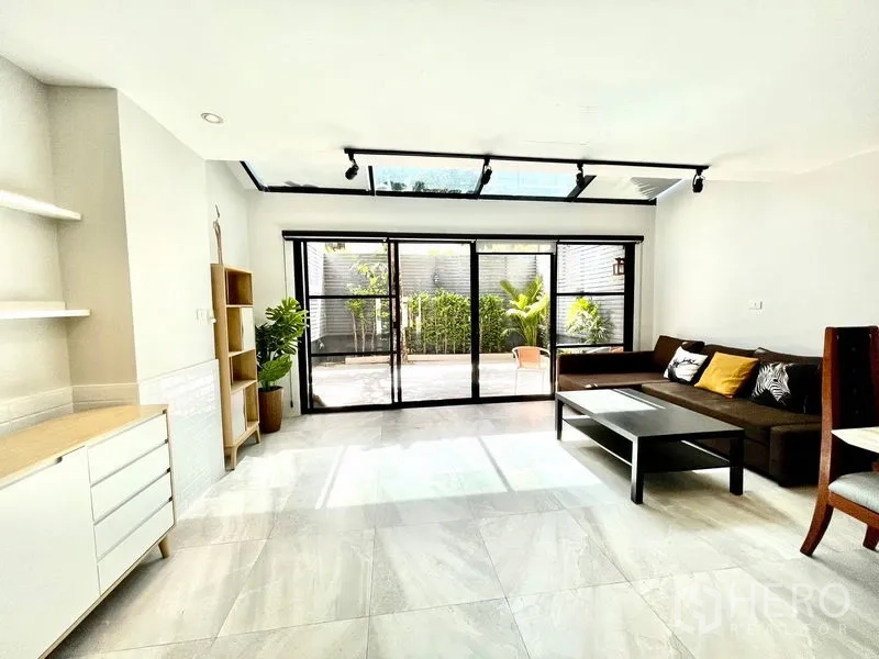 Townhouse for rent in Khlong Toei, Bangkok - Living room facing large sliding glass and patio under a skylight roof.