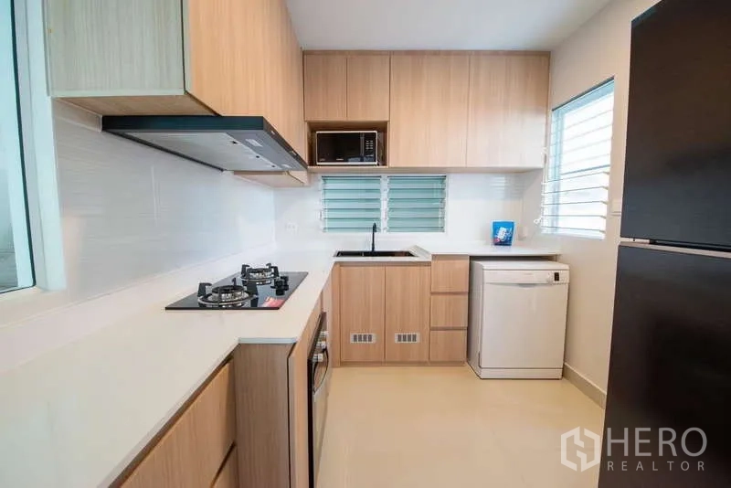 Detached House for rent in Bang Phli, Samut Prakan - Modern L-shaped kitchen with gas hob, oven, dishwasher and wood cabinets.