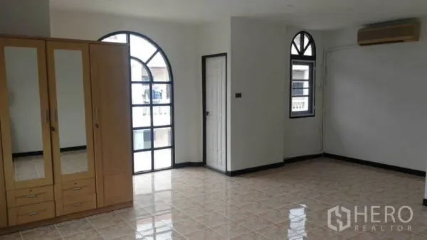 Townhouse for rent in Khlong Toei, Bangkok - Spacious room with arched windows, tiled floor and a wooden wardrobe.