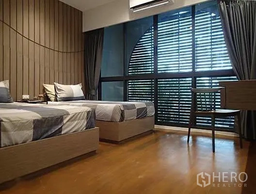 Townhouse for rent in Watthana, Bangkok - Twin bedroom with wood floors, large louvered windows, desk, and beds.