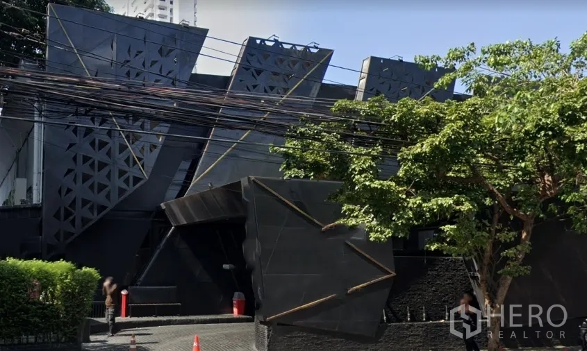 零售空间 出租在Watthana, Bangkok - 曼谷艾卡迈区黑色现代零售建筑，几何折线立面，绿树与车道清晰可见。