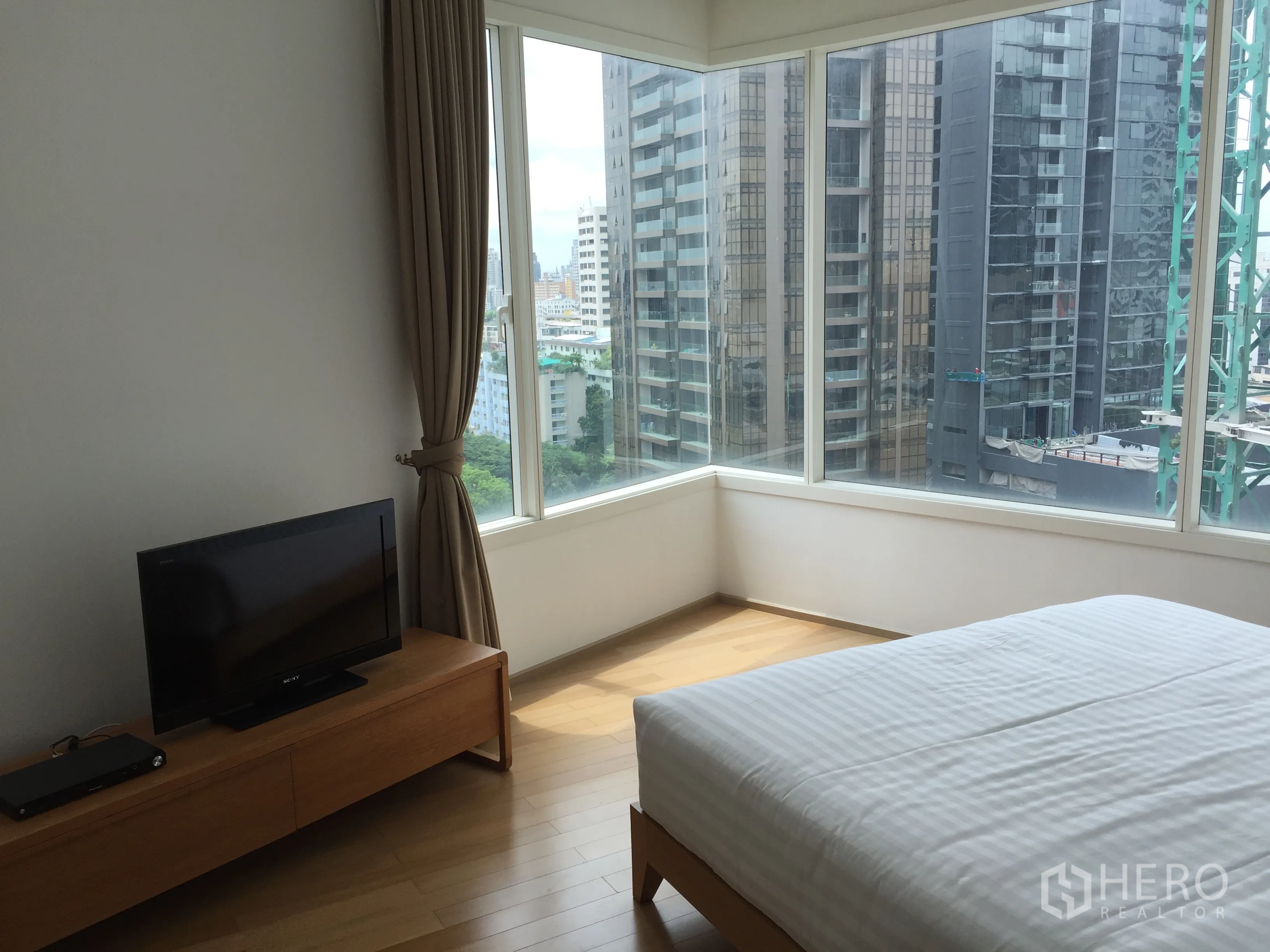 公寓 出租或出售在Watthana, Bangkok - 转角卧室，环绕落地窗享城市景观，配白色床品的床。