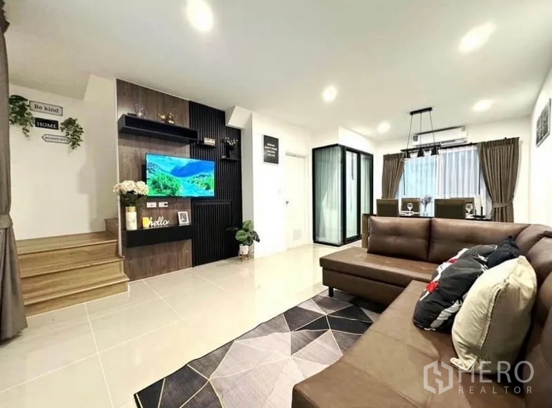 Townhouse for rent - Open-plan living and dining area with L-shaped sofa, TV feature wall, and staircase.