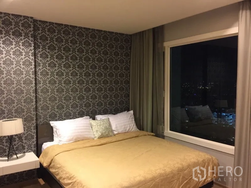 คอนโด ให้เช่าในKhlong Toei, Bangkok - ห้องนอนเตียงควีน วอลล์เปเปอร์ลาย หน้าต่างบานใหญ่พร้อมวิวเมืองยามค่ำ และผ้าม่าน