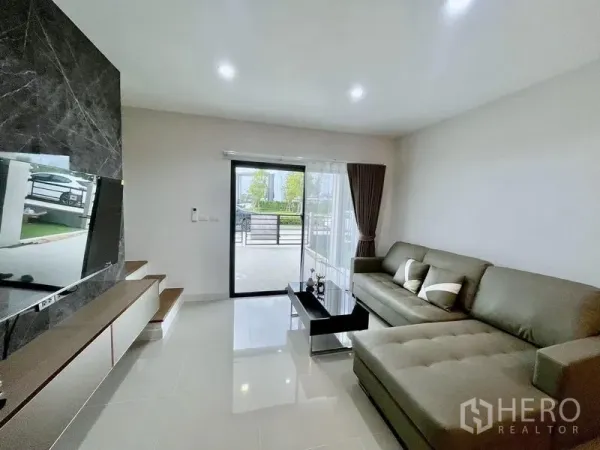 Townhouse for rent in Bang Phli, Samut Prakan - Cozy lounge with sectional sofa and glass door leading to the gated front terrace.
