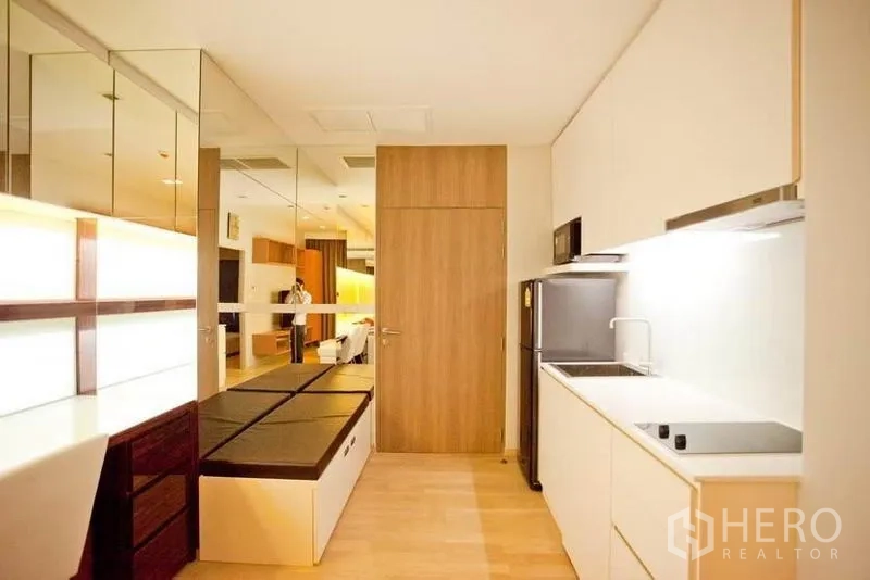 Condominium for rent or sale in Watthana, Bangkok - Kitchen corridor with glossy cabinets, refrigerator and built-in storage benches.