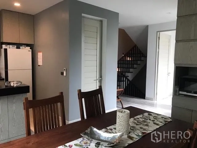 Townhouse for rent in Khlong Toei, Bangkok - Dining area with wooden table, modern kitchen corner and staircase in the background.