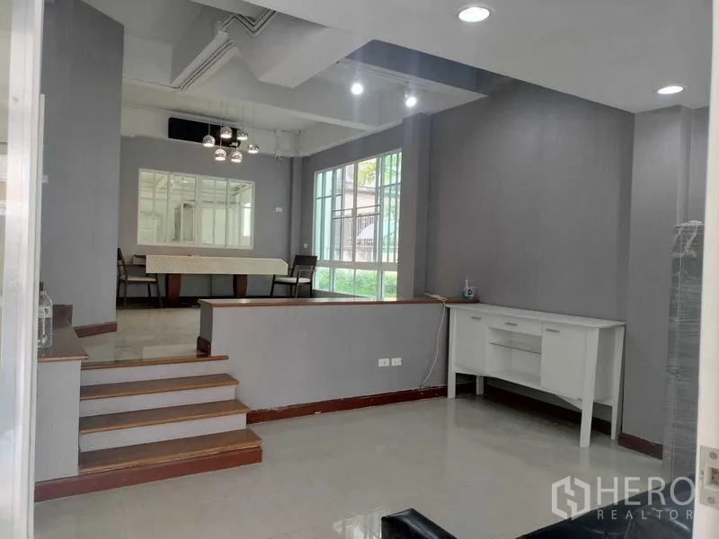 ทาวน์เฮาส์ ให้เช่าในBueng Kum, Bangkok - พื้นที่นั่งเล่นและทานอาหารแบบโอเพ่นพร้อมบันได หน้าต่างบานใหญ่ และผนังสีเทา