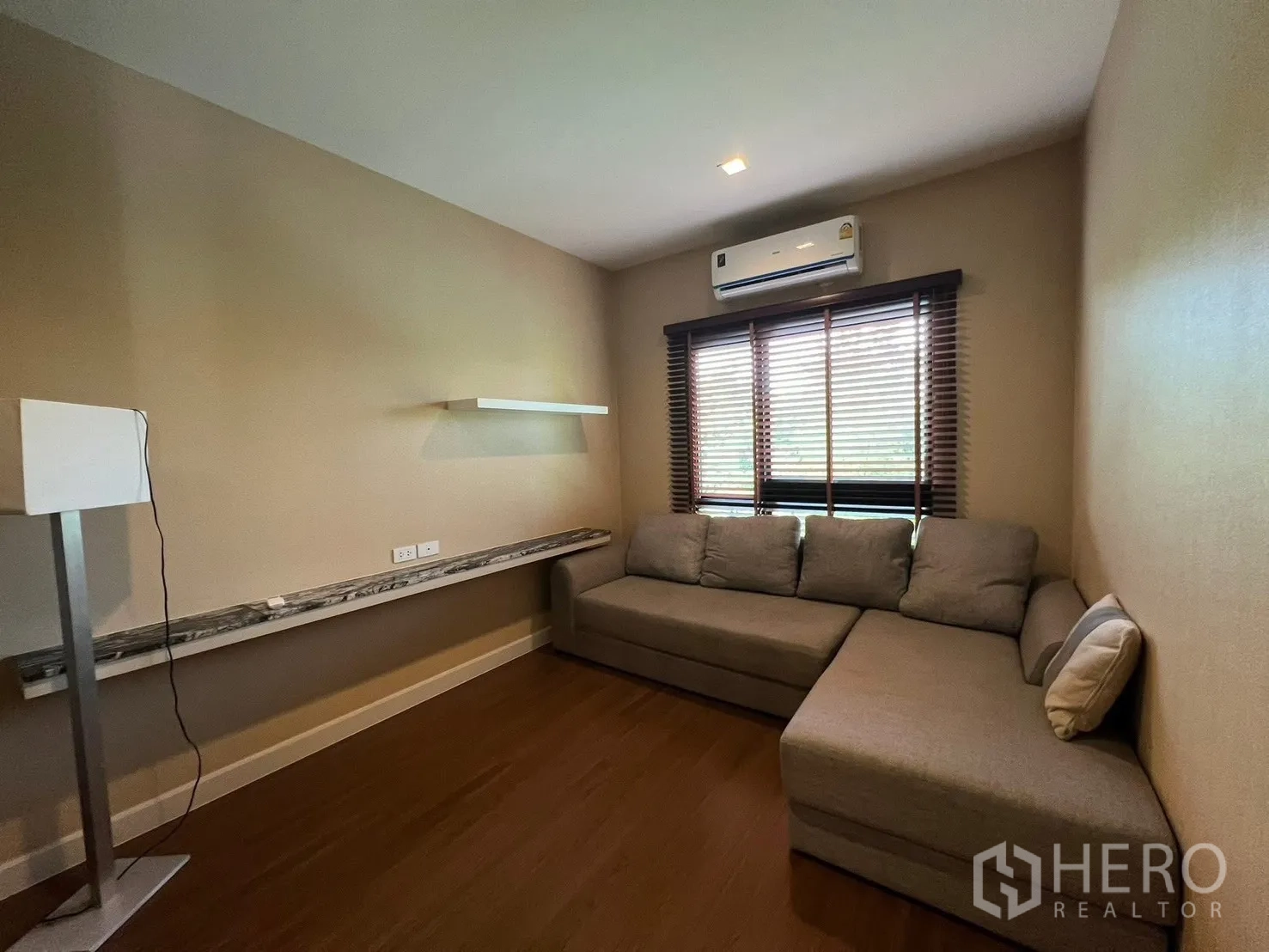 Detached House for rent in Bang Phli, Samut Prakan - Family room or study with an L-shaped gray sofa, window blinds, and a floating marble shelf.