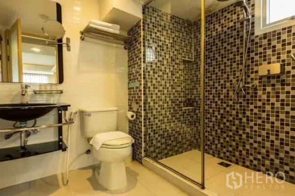 Shophouse for rent or sale in Khlong Toei, Bangkok - Modern bathroom featuring a glass-enclosed shower, mosaic tiles and a vanity basin.