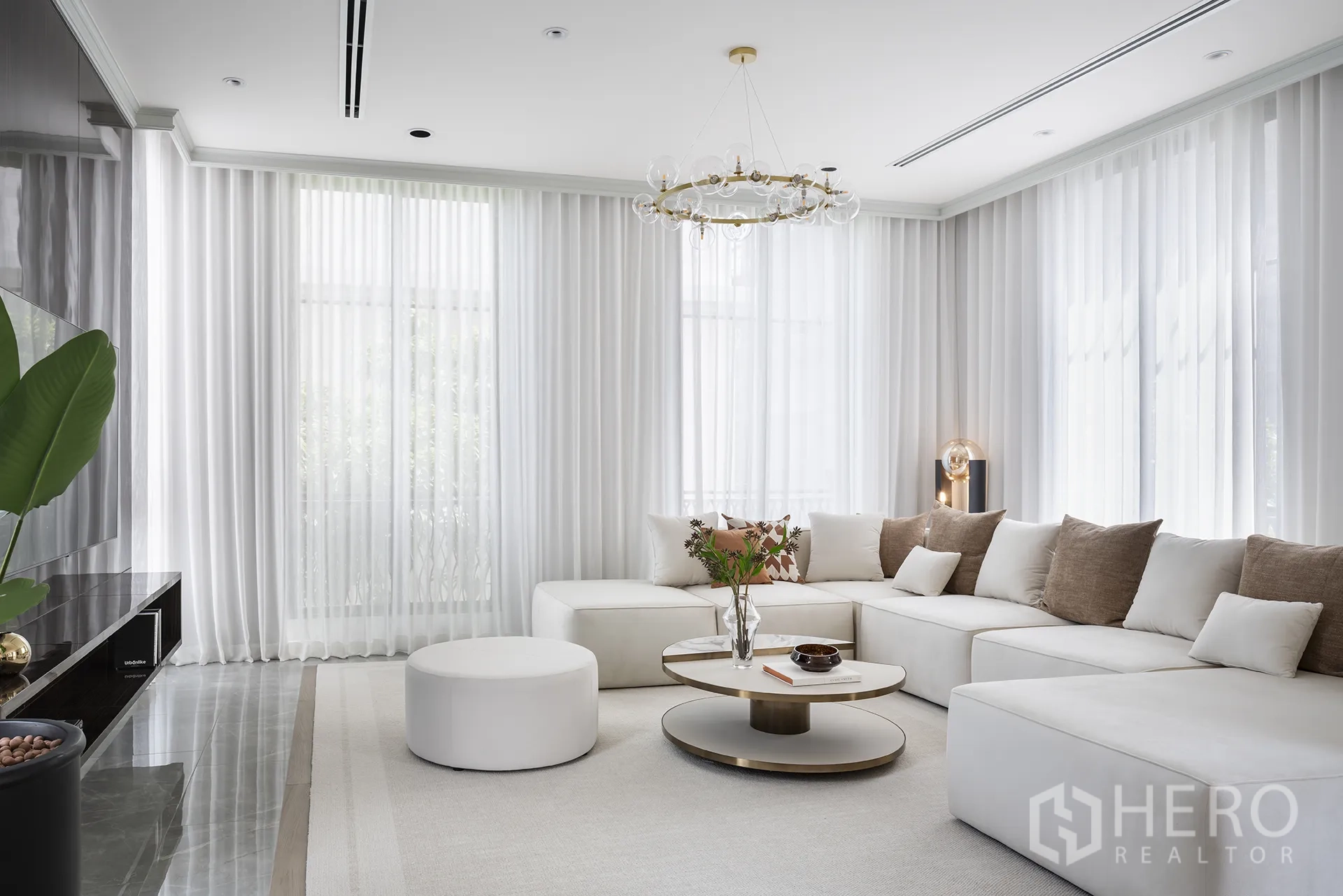 独栋房屋 for sale in Yan Nawa, Bangkok - 明亮客厅，配大号白色转角沙发、圆形茶几、现代吊灯与落地窗纱帘。