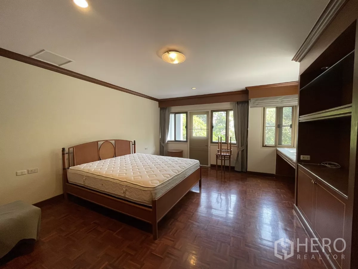 Detached House for rent in Chatuchak, Bangkok - Spacious bedroom with large windows, bed and built-in desk overlooking greenery.
