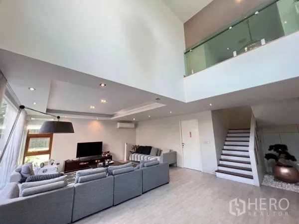 独立式住宅 出售在Chatuchak, Bangkok - 挑高客厅，L形沙发、电视柜，天花筒灯与玻璃栏板夹层。