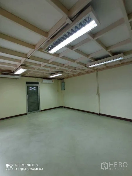 Warehouse for rent in Suan Luang, Bangkok - Compact room with roller shutter door and fluorescent lights, suitable for storage.