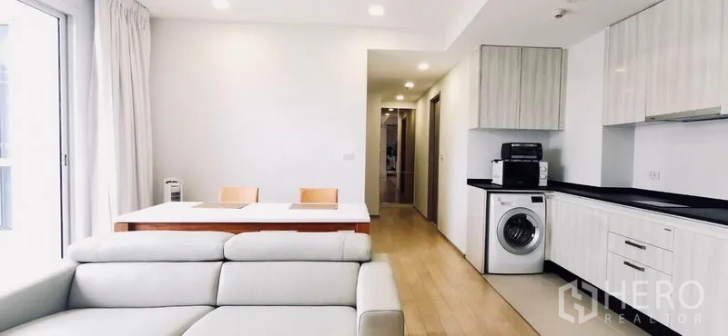 公寓 出租或出售在Watthana, Bangkok - 起居区展示沙发、餐桌和带洗衣机的厨房。