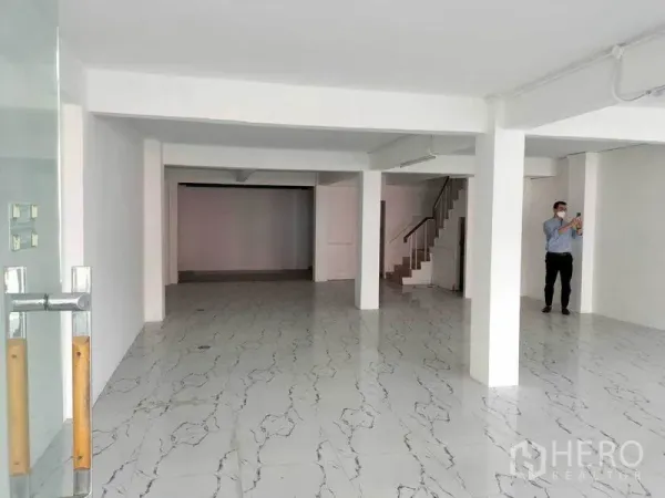 店屋 出租在Khlong Toei, Bangkok - 一层临街铺面，白色墙面、仿大理石地砖、立柱与玻璃入口。